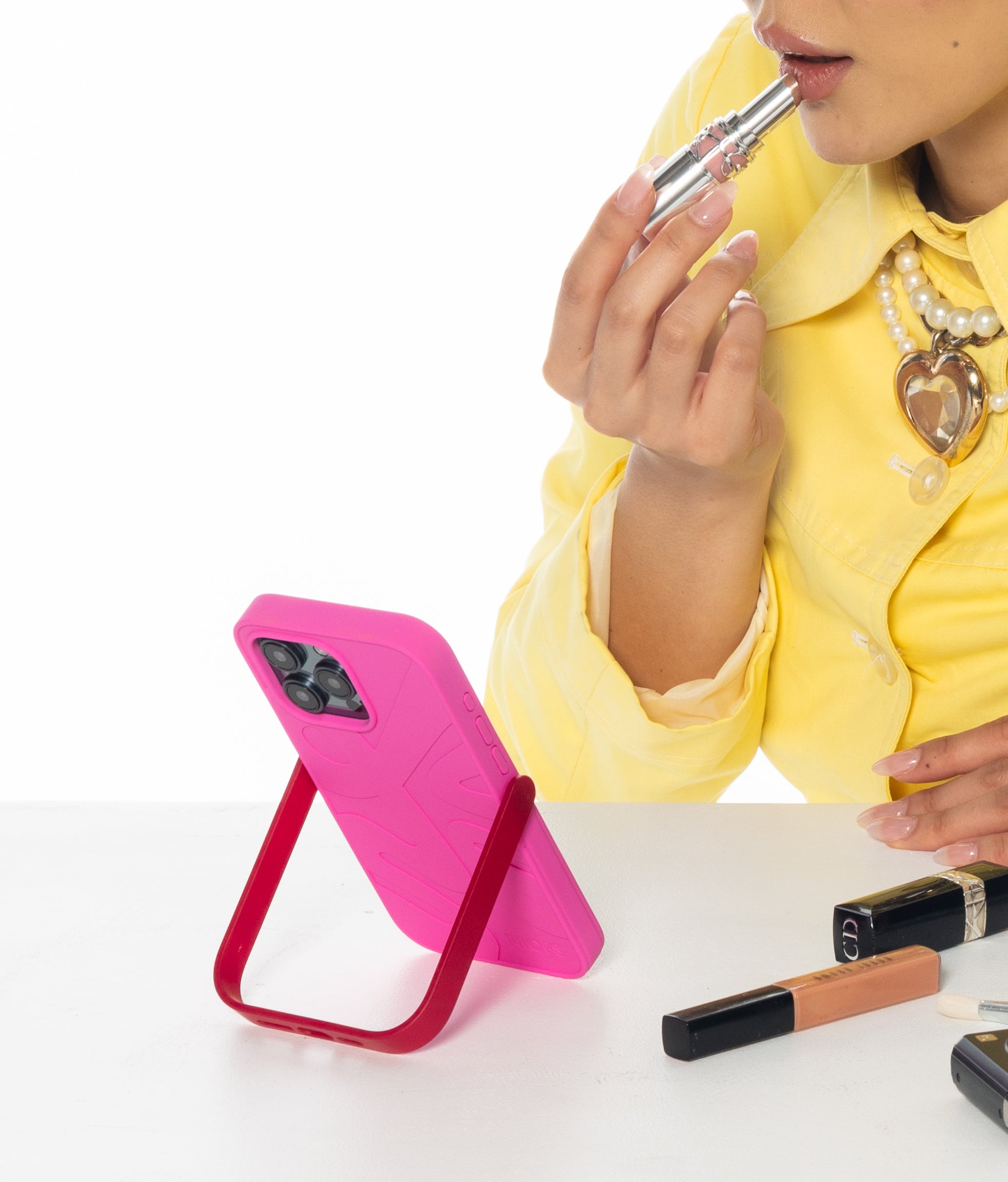 Person applying makeup with a pink PROPS phone stand case and various lip products on a white surface.