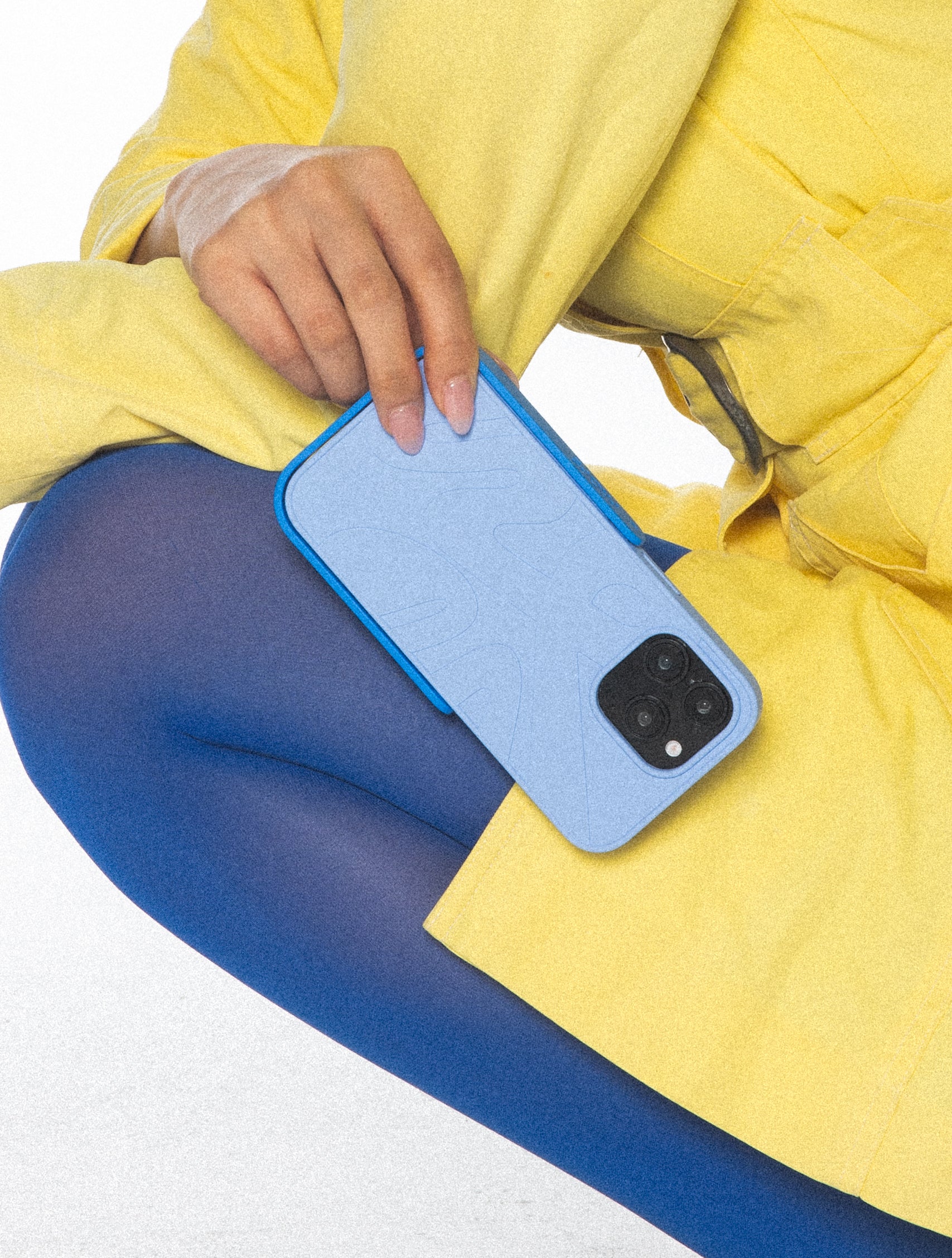 Person wearing a yellow jacket and blue leggings holding a blue PROPS phone case.