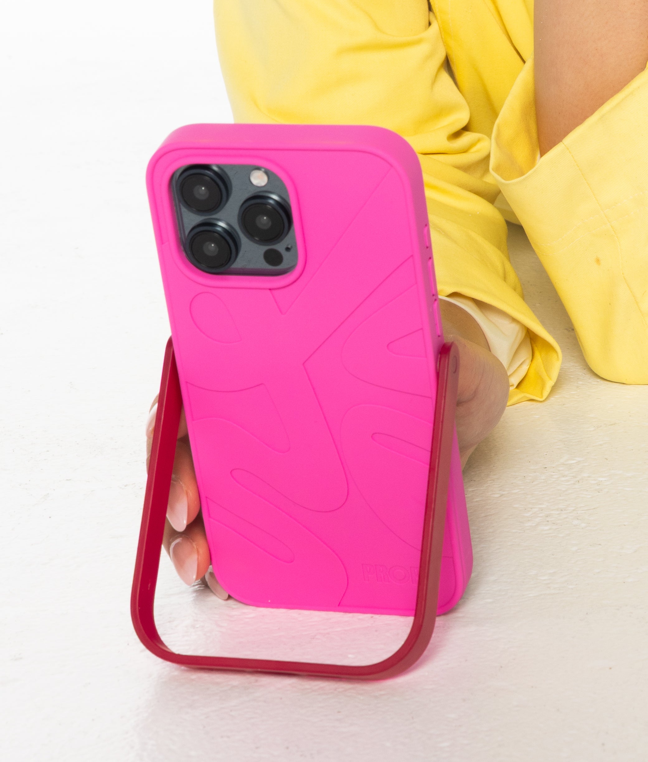 Pink PROPS phone case with a stand feature held by a person wearing yellow pants.