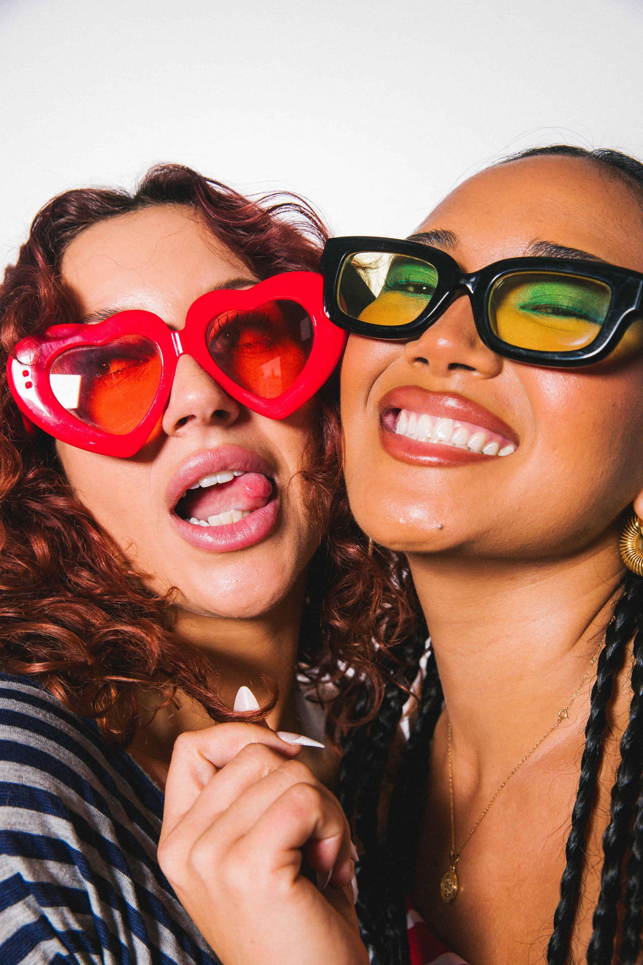Two women wearing colorful sunglasses against a white background