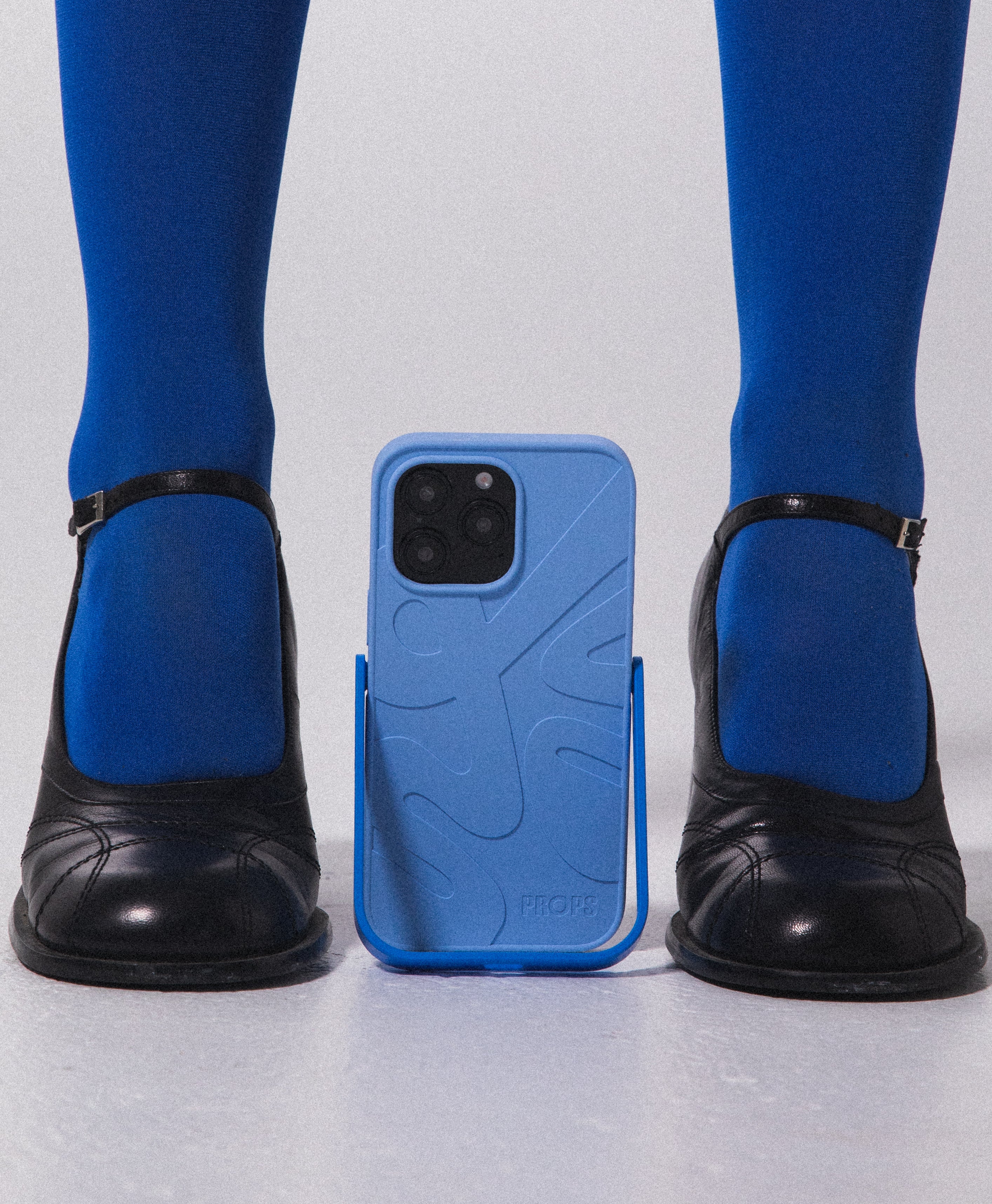 Blue PROPS phone case with a stand, between black shoes on a white background