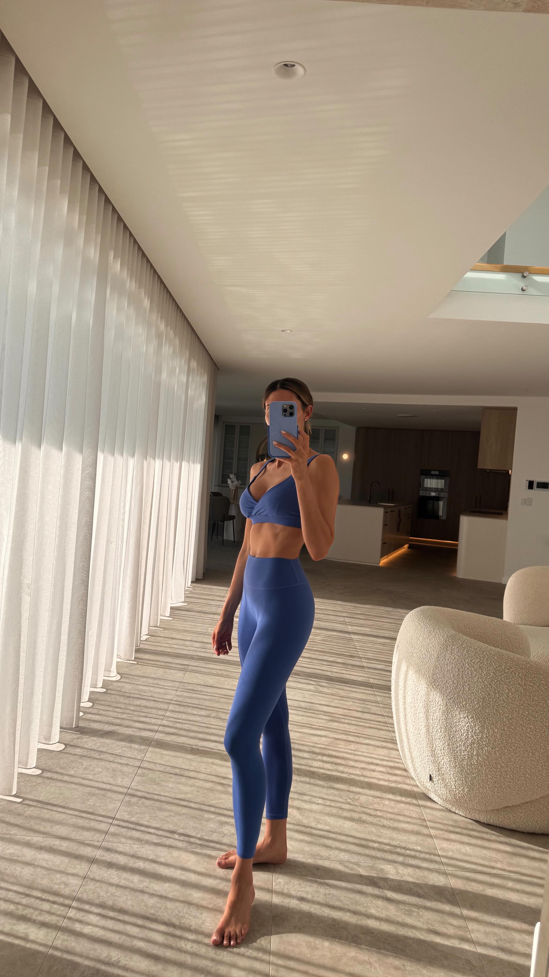 Person taking a mirror selfie in a blue athletic outfit in a modern interior setting.