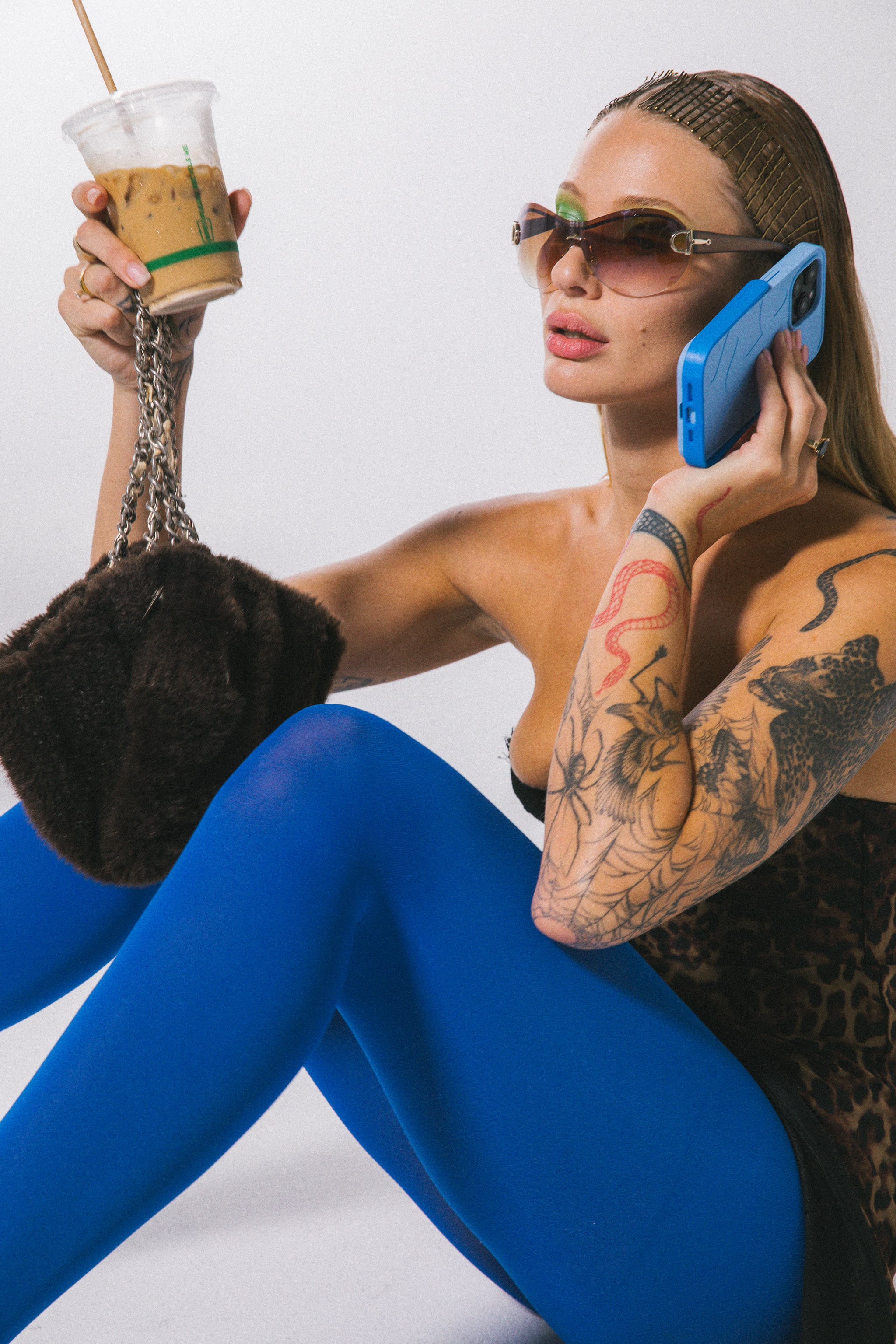 Woman in blue leggings holding a drink and phone against a white background