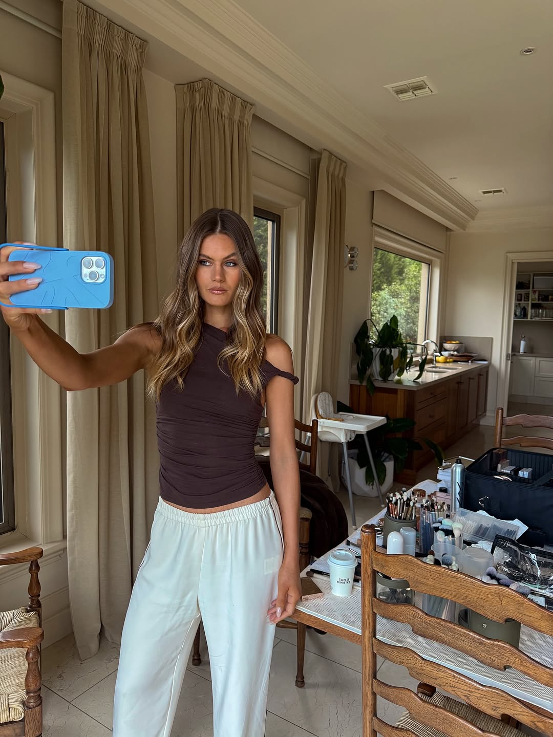 Woman taking a selfie with a PROPS case in a modern living room with a kitchen in the background.
