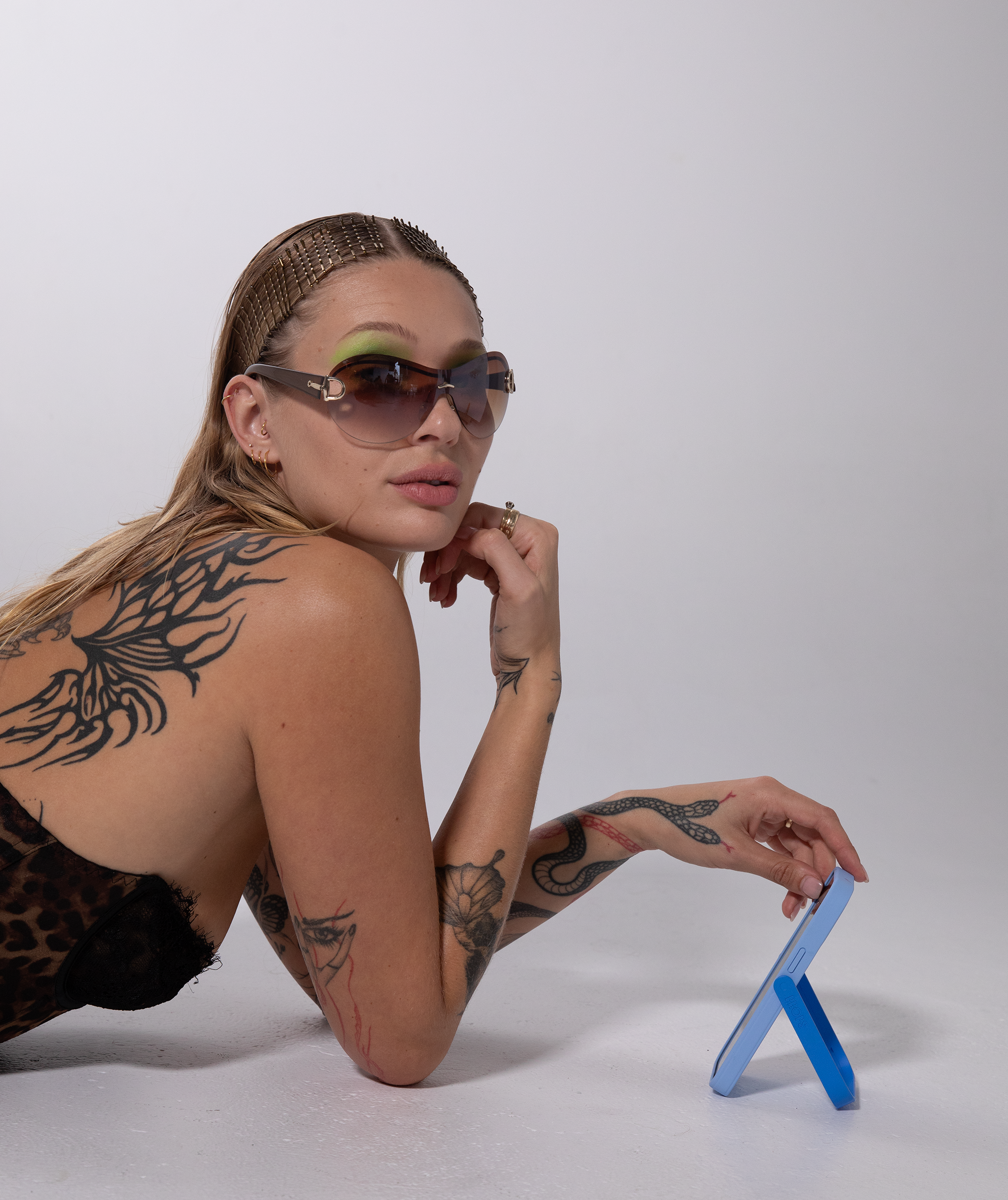 Woman with tattoos wearing sunglasses and a leopard print top, sitting on a white surface with a blue PROPS phone case